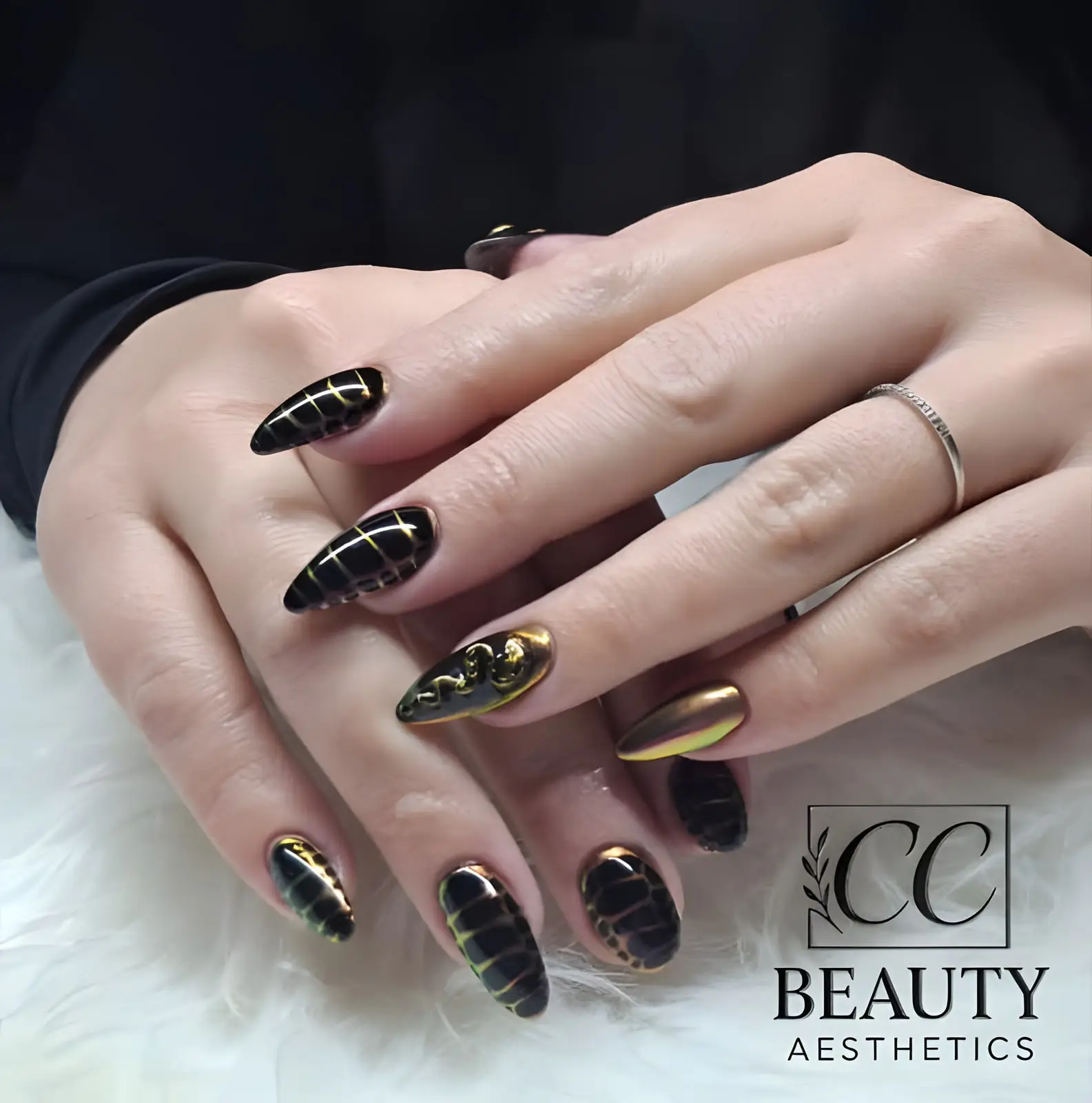 Black almond nails with gold chrome lines, one with raised gold art